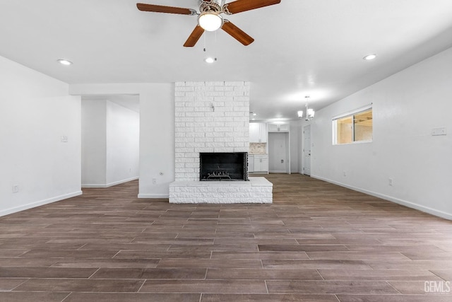 unfurnished living room with wood-type flooring, a fireplace, and ceiling fan with notable chandelier