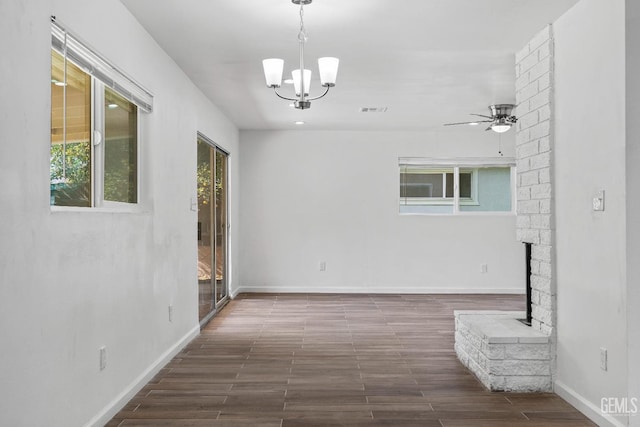 unfurnished room featuring a brick fireplace, dark hardwood / wood-style floors, and ceiling fan with notable chandelier