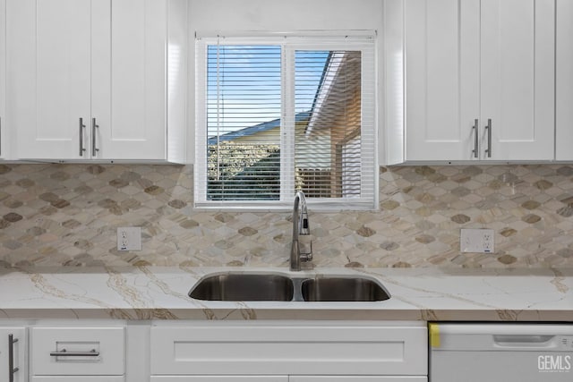 kitchen with a wealth of natural light, dishwasher, sink, white cabinets, and light stone countertops