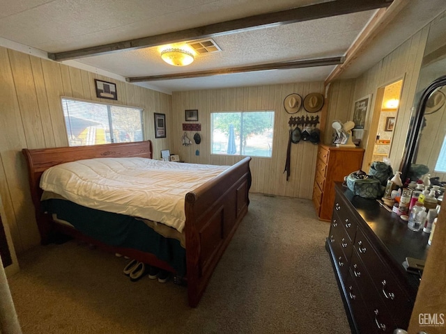 bedroom with a textured ceiling, light colored carpet, wood walls, visible vents, and beamed ceiling