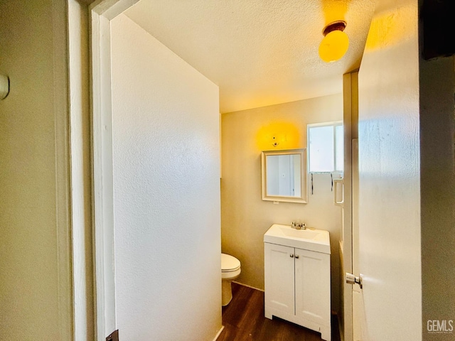 half bathroom featuring toilet, a textured ceiling, wood finished floors, and vanity
