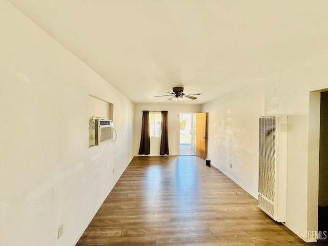 unfurnished room featuring an AC wall unit, a heating unit, ceiling fan, and wood finished floors