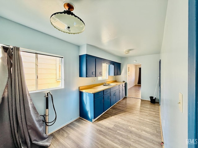 kitchen with light wood finished floors, light countertops, blue cabinetry, and a sink