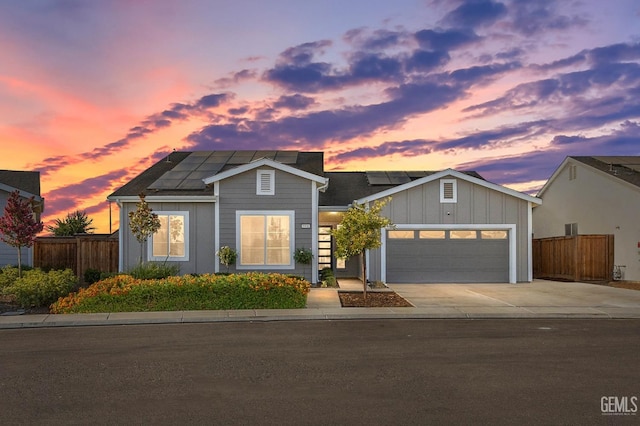 view of front of house featuring concrete driveway, solar panels, and fence