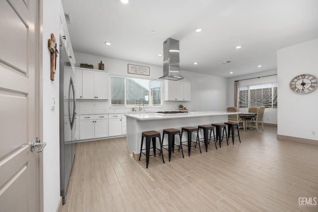 kitchen with island range hood, a kitchen island, a breakfast bar, light countertops, and white cabinetry