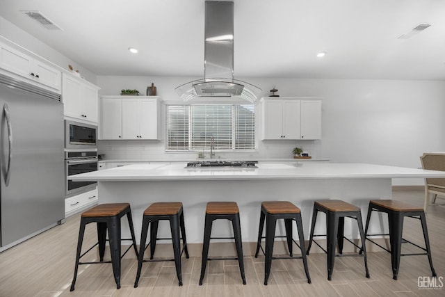 kitchen with built in appliances, a spacious island, white cabinets, light countertops, and island exhaust hood