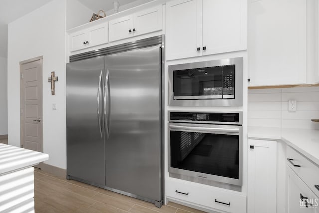 kitchen featuring built in appliances, white cabinetry, light countertops, wood tiled floor, and tasteful backsplash