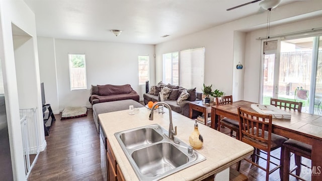 kitchen featuring tile countertops, an island with sink, visible vents, dark wood-style flooring, and a sink