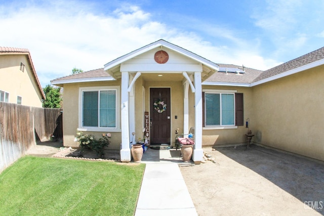 property entrance featuring roof with shingles, fence, a lawn, and stucco siding