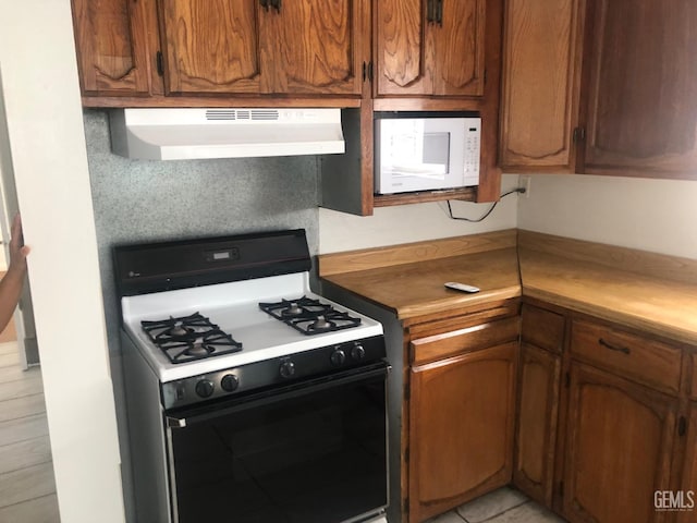 1543 Sycamore Dr, Wasco, CA 93280 - kitchen with range with gas stovetop, extractor fan, white microwave, and brown cabinetry