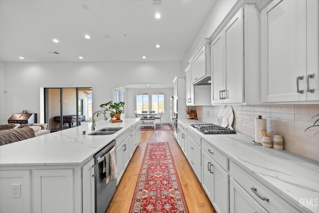 kitchen featuring white cabinets, stainless steel appliances, light stone countertops, and a center island with sink