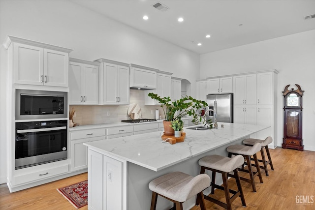 kitchen featuring a breakfast bar, a center island with sink, sink, appliances with stainless steel finishes, and white cabinetry