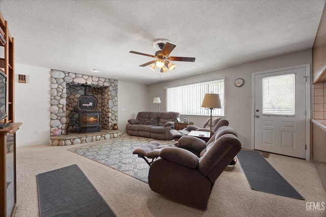 living area with a textured ceiling, a ceiling fan, carpet, and a wood stove