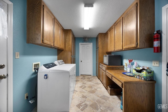 laundry area with cabinet space, washing machine and clothes dryer, a desk, a textured ceiling, and stone finish flooring