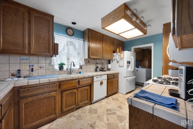 kitchen featuring white appliances, a sink, washer and dryer, tasteful backsplash, and tile counters