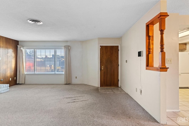 spare room with a textured ceiling, wooden walls, and light carpet