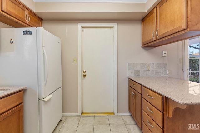 kitchen featuring kitchen peninsula, light tile patterned floors, ornamental molding, white refrigerator, and light stone counters