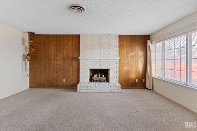 unfurnished living room featuring light colored carpet, wooden walls, plenty of natural light, and a fireplace