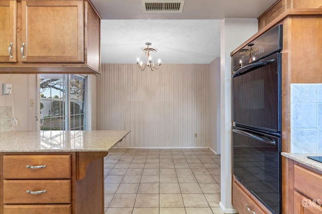 kitchen with double oven, light tile patterned flooring, a chandelier, and light stone counters