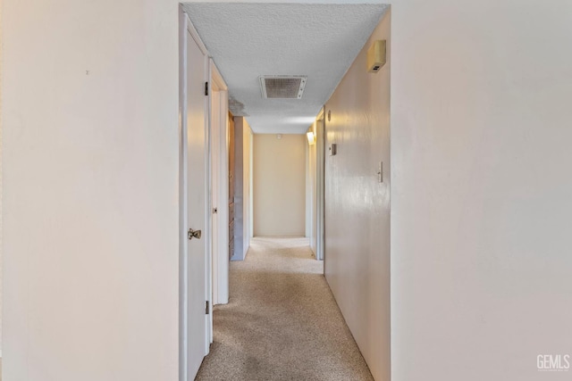 corridor featuring a textured ceiling and light carpet