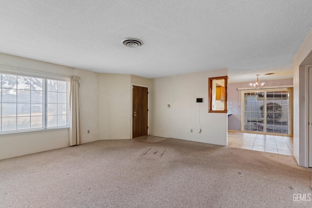 spare room featuring a textured ceiling, light colored carpet, and an inviting chandelier