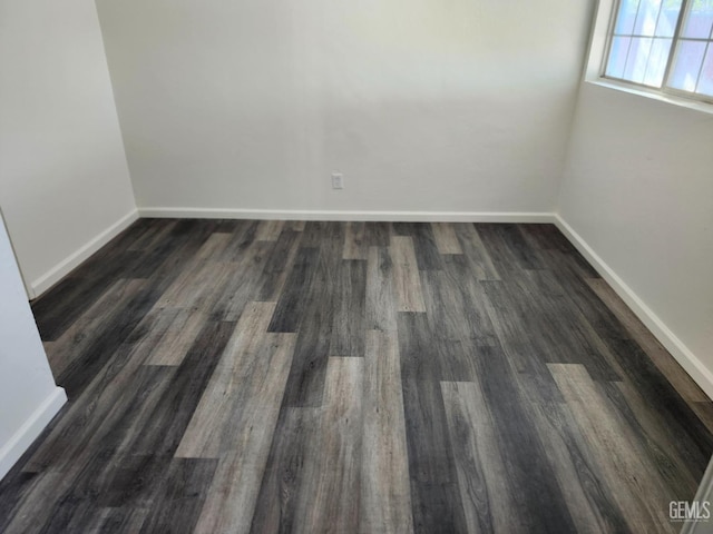 spare room featuring dark wood-type flooring and baseboards