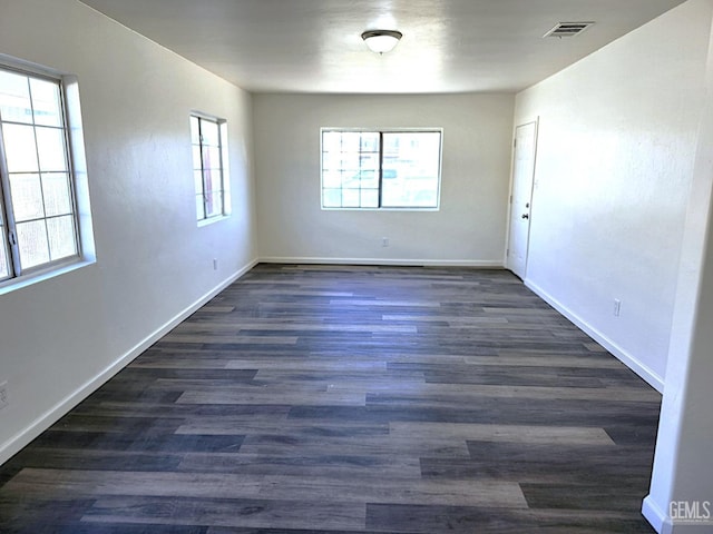 empty room with dark wood-style floors, a wealth of natural light, visible vents, and baseboards