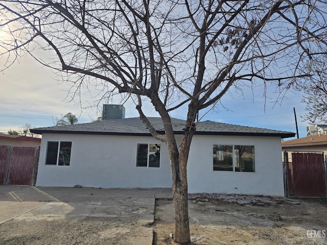 view of side of property with roof with shingles, fence, and stucco siding