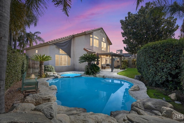 pool at dusk with an in ground hot tub and a patio area