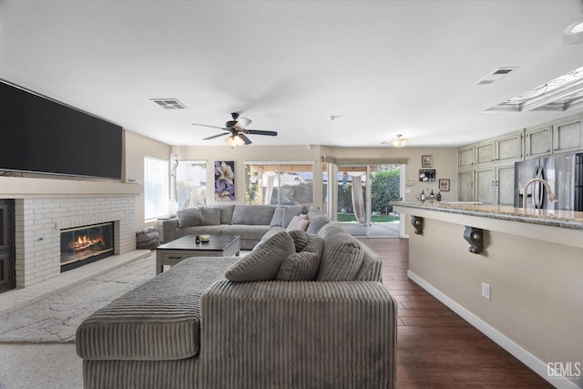 living room with ceiling fan, a brick fireplace, and dark hardwood / wood-style flooring