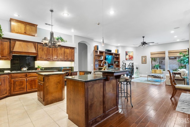 kitchen featuring a kitchen bar, a center island, custom range hood, pendant lighting, and ceiling fan with notable chandelier