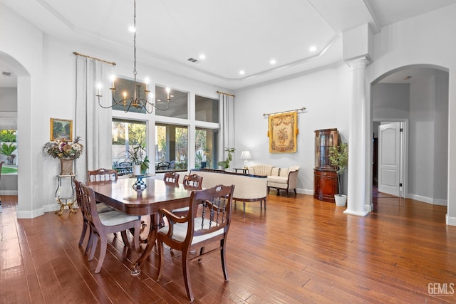 dining area with hardwood / wood-style flooring, a high ceiling, a notable chandelier, and ornate columns