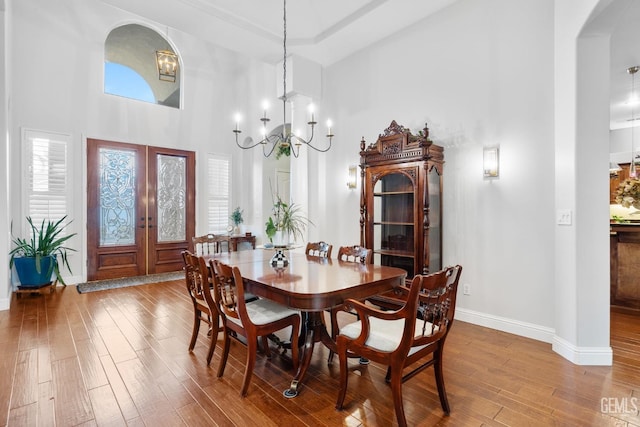 dining area with wood-type flooring, french doors, a chandelier, and a high ceiling