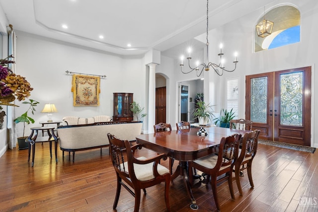 dining room with ornate columns, a towering ceiling, dark hardwood / wood-style flooring, a notable chandelier, and french doors