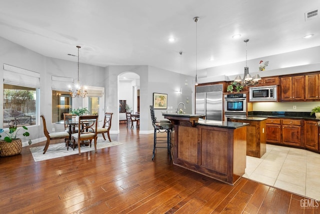 kitchen featuring an island with sink, pendant lighting, built in appliances, and a notable chandelier