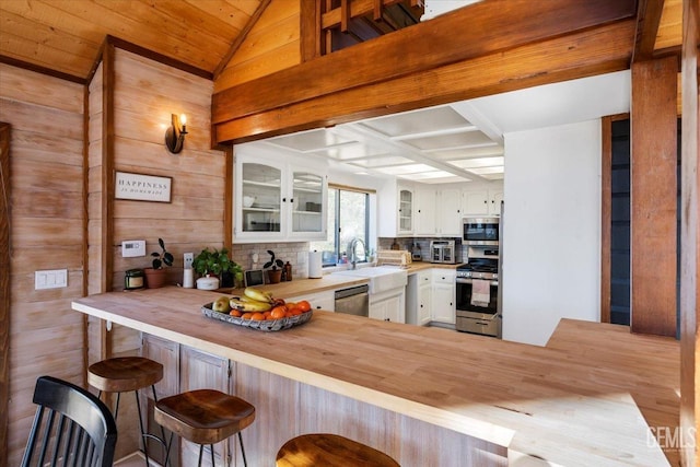 kitchen with backsplash, appliances with stainless steel finishes, glass insert cabinets, white cabinets, and wood counters