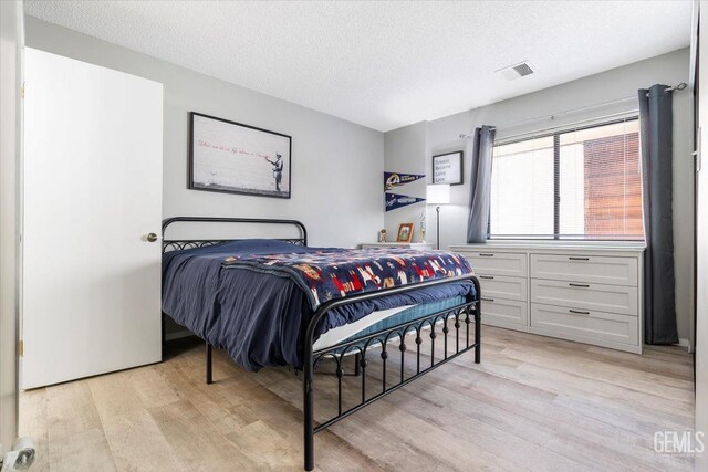 bedroom with light wood-style floors, visible vents, and a textured ceiling