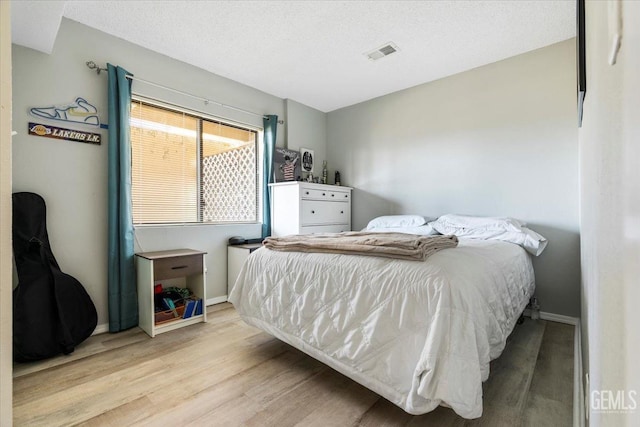 bedroom featuring a textured ceiling, wood finished floors, visible vents, and baseboards