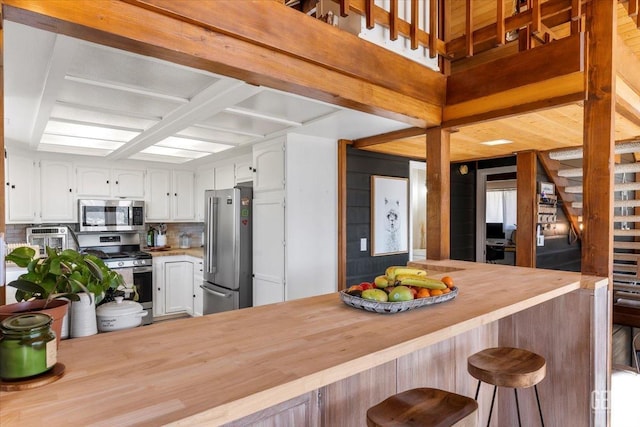 kitchen featuring butcher block counters, decorative backsplash, appliances with stainless steel finishes, white cabinets, and a kitchen breakfast bar