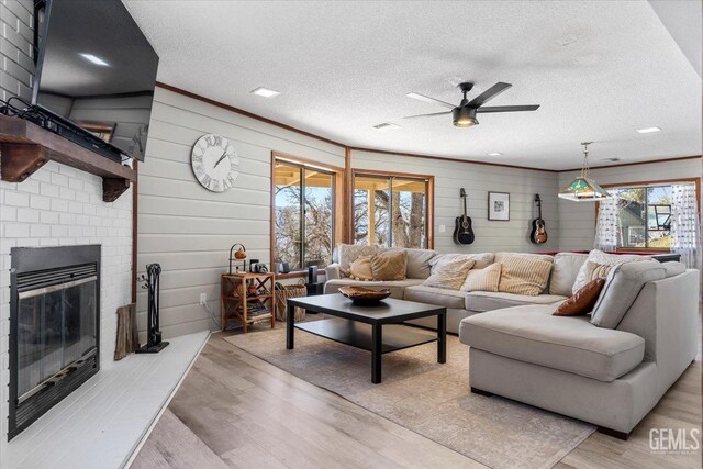 living area featuring a brick fireplace, plenty of natural light, light wood-style flooring, and a textured ceiling