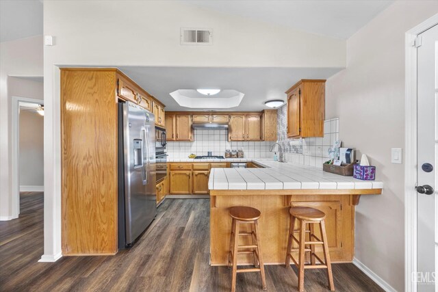 9913 Mark Twain Ave, Bakersfield, CA 93312 - kitchen featuring stainless steel appliances, a peninsula, dark wood-style flooring, backsplash, and brown cabinets