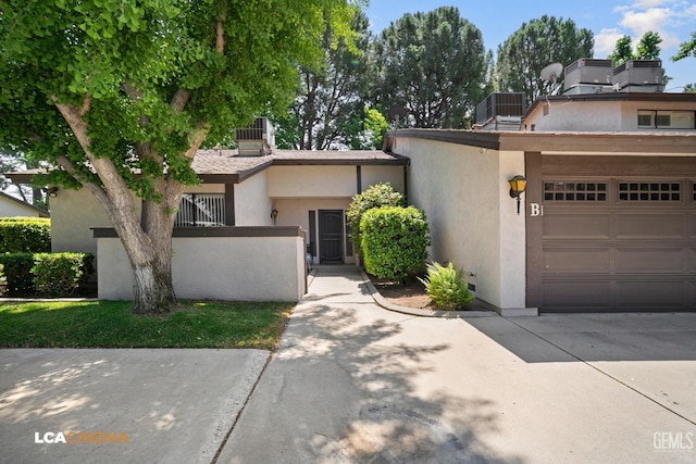 view of front of property with concrete driveway, central air condition unit, stucco siding, and fence
