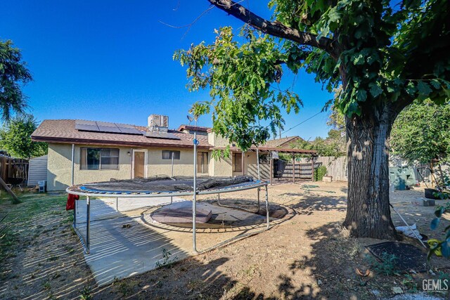 6901 Shelby Loop, Bakersfield, CA 93309 - back of house featuring a trampoline, stucco siding, roof mounted solar panels, and a fenced backyard