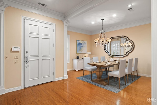 dining room featuring crown molding, a chandelier, light hardwood / wood-style floors, and ornate columns