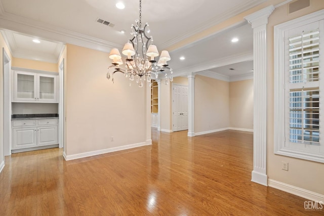 spare room featuring ornate columns, a notable chandelier, crown molding, and light wood-type flooring