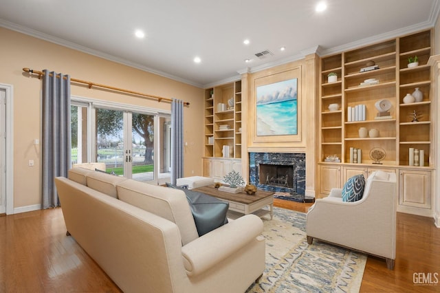 living room featuring light hardwood / wood-style floors, ornamental molding, a premium fireplace, and french doors