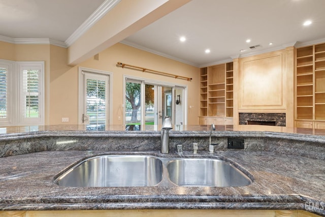 kitchen featuring built in features, light brown cabinetry, sink, dark stone countertops, and crown molding