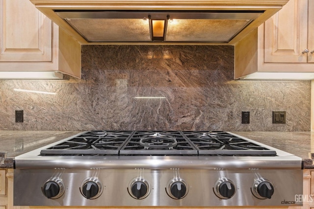 kitchen featuring light brown cabinetry, tasteful backsplash, ventilation hood, dark stone countertops, and stainless steel gas stovetop