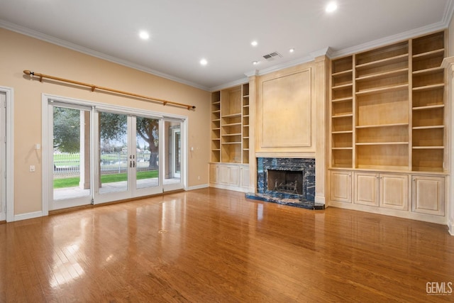 unfurnished living room featuring ornamental molding, wood-type flooring, a high end fireplace, and french doors