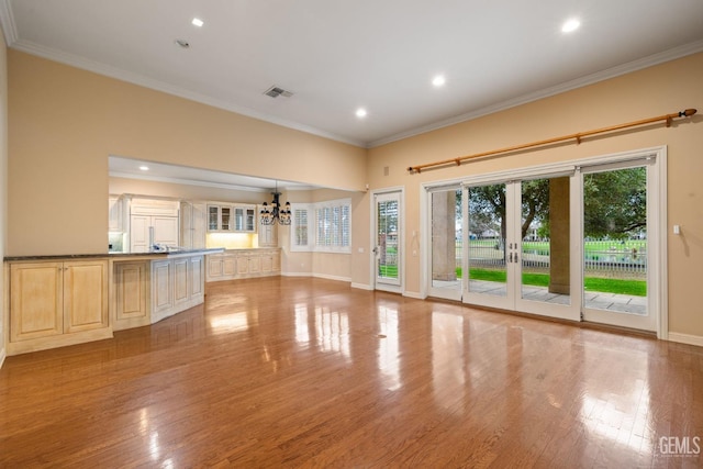 unfurnished living room with a notable chandelier, ornamental molding, french doors, and light wood-type flooring